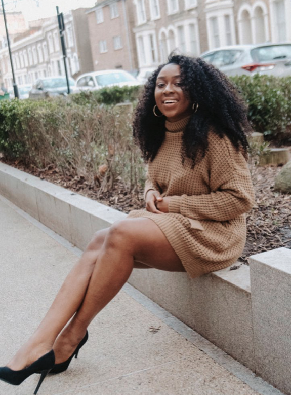 Marcelle Adrianna seated outdoors in a camel knit dress